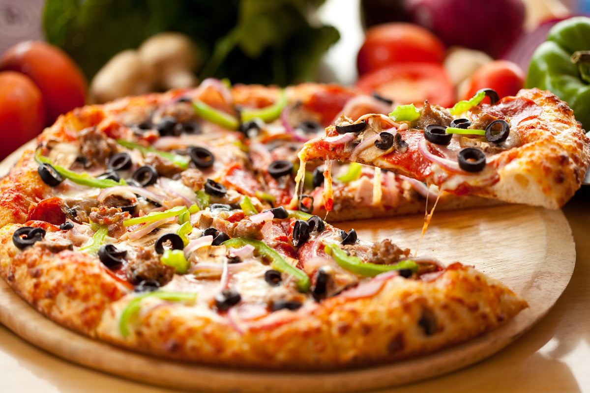 Frische Pizza mit Paprika, Oliven, Käse und weiteren Zutaten auf einem Holzbrett serviert