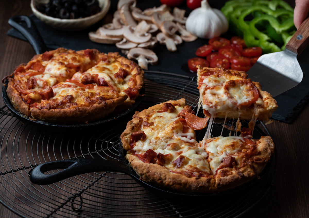 Zwei frisch gebackene Pan Pizzen von Pan Pizza 2Go mit Zutaten im Hintergrund