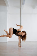 Poledancerin zeigt eine einarmige Halteposition an der Stange mit beeindruckender Körperspannung