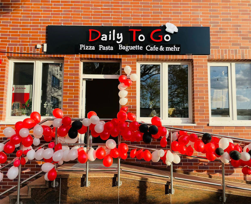 Feierlich geschmückter Eingang der Pizzaria Daily To Go in Düsseldorf mit roten und weißen Ballons