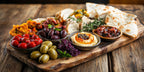 Mediterrane Vorspeisenplatte mit Oliven, Hummus, Käse, Brot und Antipasti auf Holzbrett